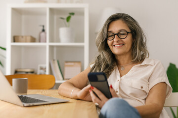 Happy woman sitting and using smart phone at home