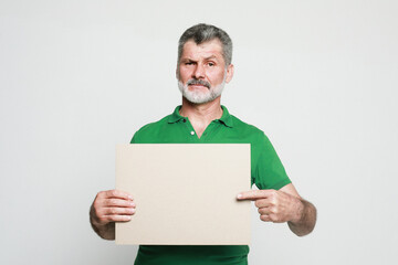 Senior handsome man with mustache and beard wearing green shirt holds the white sign in a studio