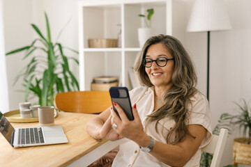 Obraz na płótnie Canvas Smiling woman video chatting via smartphone at home