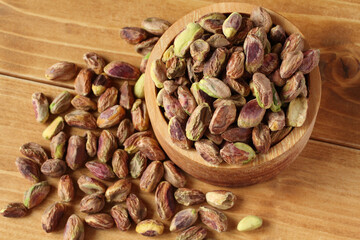 Peeled salted pistachios in a wooden bowl on a wooden table.