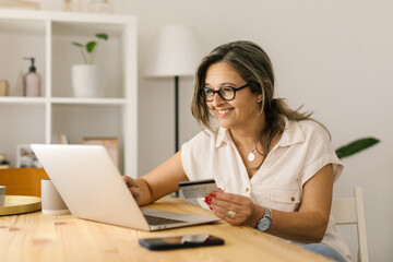 Happy boomer female shopping online via laptop at home