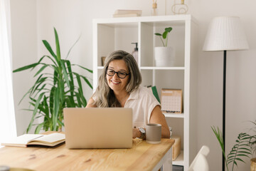 Happy mature woman working in home office via computer