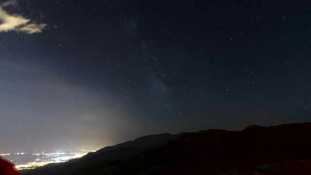 Night time lapse shot with milky way and stars and mountain Monte Canarinco near Bastia. Lights of a city Biguglia on bottom left