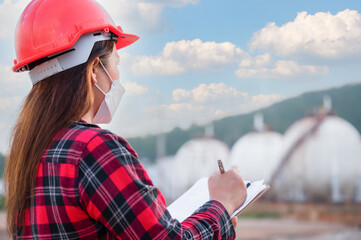 Asian woman petrochemical engineer wearing safety helmet standing holding a clipboard with checking...