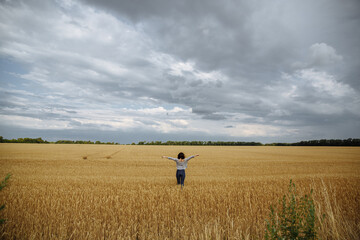 A girl in a field of yellow wheat on the background of a rainy sky