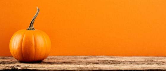 Decorative pumpkin on wooden table on orange background. Banner design with copy space....