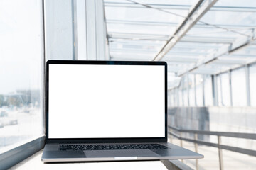 Fototapeta premium Laptop with white screen in railway station. Empty copy space, blank screen mockup. Soft focus laptop in railway station background. Travel, study and work outside office concept