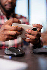 Young man playing online video games on virtual technology, holding smartphone to have fun wth game play on internet. Enjoying gaming competition with mobile phone, working remotely. Close up.