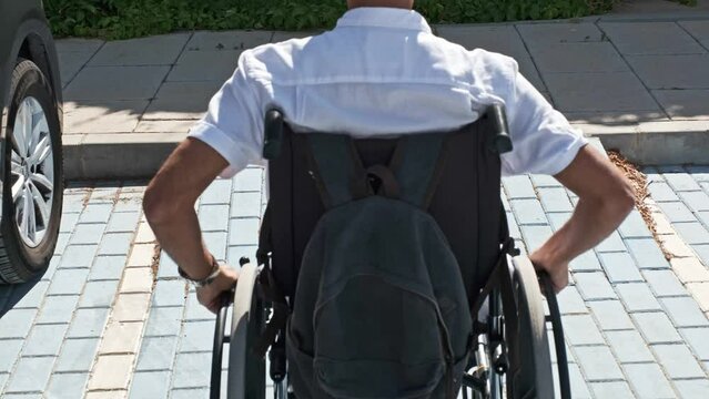dark-haired man in a white shirt from the back in a wheelchair walking up a ramp next to his car parked in an accessible parking space