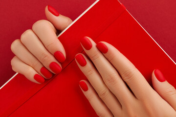 Female hand with manicure holding notepad. Red matt nail design - obrazy, fototapety, plakaty