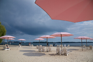 Fototapeta na wymiar Pink beach umbrellas and Adirondack chairs at the sunny lakeshore