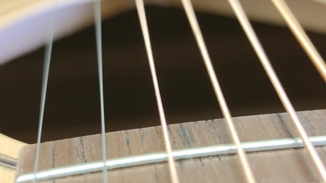 Guitar strings vibrate when touched. Close-up on metal strings. They have different thickness and different tone of sound. When touched, the strings begin to vibrate and make a sound.
