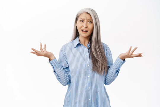 Confused Japanese Middle Aged Woman Looking Questioned And Frustrated, Shrugging Shoulders With Disappointed Face Expression, Asking What, Standing Over White Background