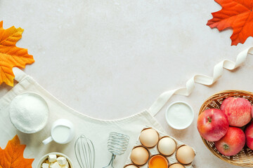 Autumn fall baking food background with flour, milk, eggs, apples, butter, whisk for beating eggs on the apron. Decorated with fallen leaves. Cooking apple pie. Autumn baking sale concept