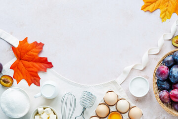 Autumn fall baking food background with flour, milk, eggs, plums, butter, whisk for beating eggs on the apron. top view. Decorated with fallen leaves. Cooking plums pie. Background for recipe 