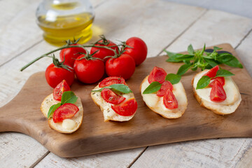 Italian homemade bruschetta with roasted cherry tomatoes, mozzarella cheese, basil and herbs on a cutting board