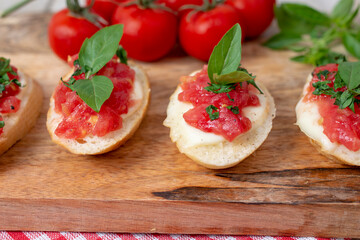 Homemade bruschetta with tomatoes, mozzarella cheese  and basil on cutting board on a wooden background. Traditional italian appetizer or snack, antipasto. Top view