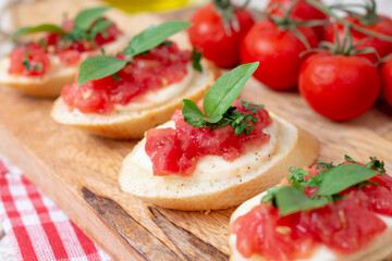 Italian homemade bruschetta with roasted cherry tomatoes, mozzarella cheese, basil and herbs on a cutting board