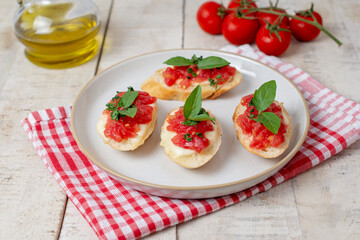 Traditional homemade roasted bruschetta with mozzarella, cherry tomatoes and basil in a white plate on a wooden background. Top view