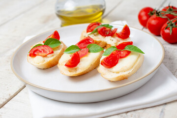 Traditional homemade roasted bruschetta with mozzarella, cherry tomatoes and basil in a white plate on a wooden background. Top view