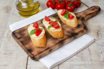 Homemade bruschetta with tomatoes, mozzarella cheese  and basil on cutting board on a wooden background. Traditional italian appetizer or snack, antipasto. Top view, 