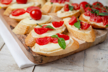Italian homemade bruschetta with roasted cherry tomatoes, mozzarella cheese, basil and herbs on a cutting board