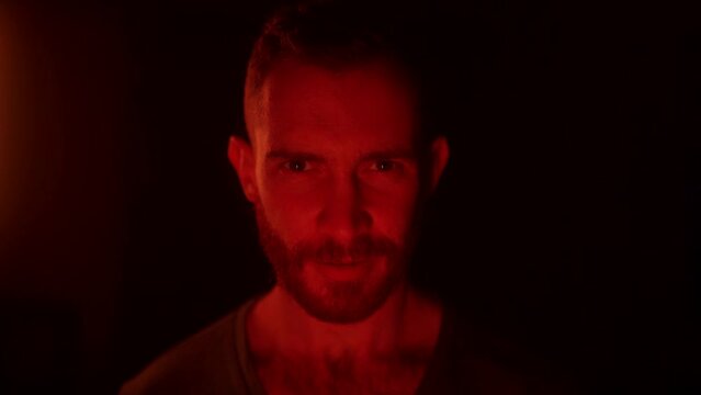 Angry man open eyes, awakes in hell, looking at camera with fury, rage, his face lit with fire flames, grief, sorrow. Male starring at enemy on war with aggresive emotions and insane devilish look.