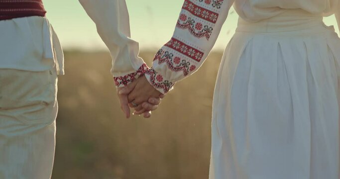 Close-up, a Ukrainian man holding the hand of a Slavic woman, walking together across the field. People in embroidered shirts hold hands, friendship of peoples. 4k, ProRes