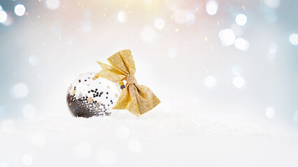 Christmas ball for the tree.A silvery ball with a gold bow lies in the snow on a light background.