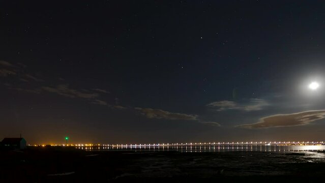 Night time lapse shot of port entrance of Saint Trojan les Bains while low water at night with stars and moon moving through the sky.