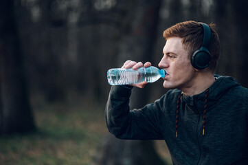 Redhead young man drinking water while training outside