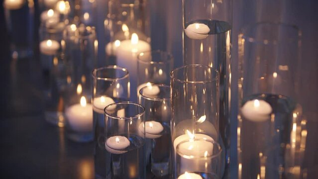 Floating candles burning in glass vases filled with water near white wedding table tablecloth. Boho rustic decor. Birthday party decoration. Sorrow, funeral or mourning candles concept.