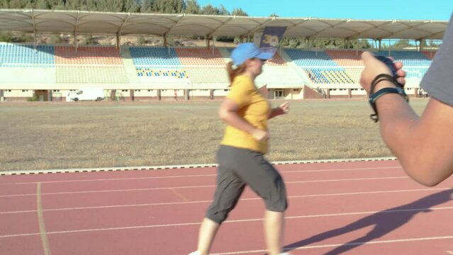 overweight woman runs in the stadium wants to lose weight, running training in the stadium under the guidance of a coach with a stopwatch