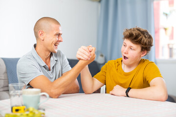 Happy smiling father and son arm wrestling at home. Fatherhood concept