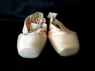 A worn pair of ballet pointe shoes on a black background