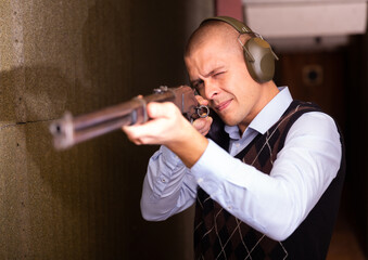 Fototapeta na wymiar Portrait of confident shooter sighting in or zeroing shotgun in shooting gallery.