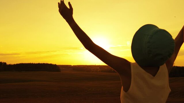 boy raises his hands to the sky on mars, boy in a hat raises hands to the sky in the field sun glare at sunset, boy praying to heaven