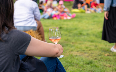 Back view of a seated female figure with a glass of wine in her hand at a picnic