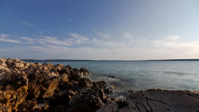 Time lapse shot of a rocky beach on the island of Pag with the island Maun in the background on a sunny summer day.