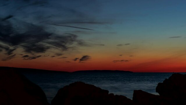 Time lapse shot of some rocks at the beach on the island of Pag with the islands Maun and Skrda while a colorful dusk with some clouds