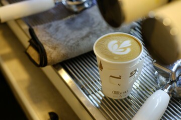coffee latte or cappuccino with latte art on top in paper take away cup well prepare by barista in small cafe at espresso machine