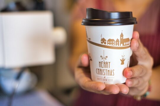 close up bokeh picture barista hand under serving hot cup of coffee in take away cup with Merry Christmas