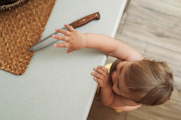 Little child reaching for knife on light countertop, above view. Dangers in kitchen - obrazy, fototapety, plakaty