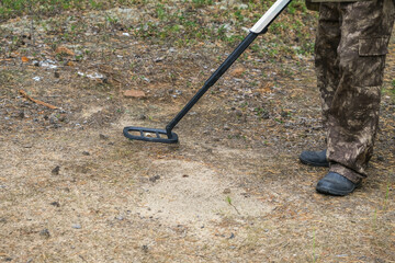 Metal detector in the forest. A man is looking for a treasure in the forest. A man in camouflage with a metal detector.
