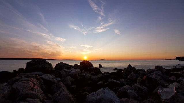 Time lapse shot of some rocks at the beach on the island of Pag with the islands Maun and Skrda while a colorful sunset with some clouds.