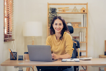 Portrait of a beautiful Asian woman looking at laptop screen while sitting at working desk in the office