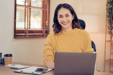 Portrait of a beautiful Asian woman looking at laptop screen while sitting at working desk in the office