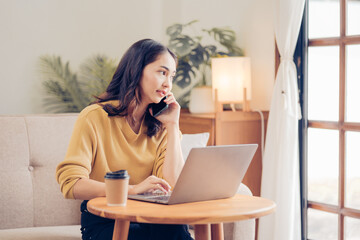 Confident pretty asian business woman working with laptop while doing some paperwork at home