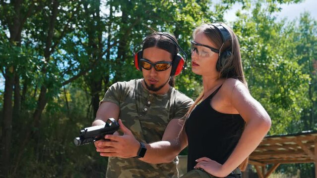 Private shooting lesson at a nearby outdoor gun range. Two people in moro military-like clothes. Caucasian male instructor and caucasian woman. Full length shot. High quality 4k footage