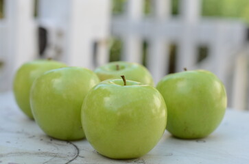 fresh green apples in a wooden basket outdoors with pretty white fence in the background